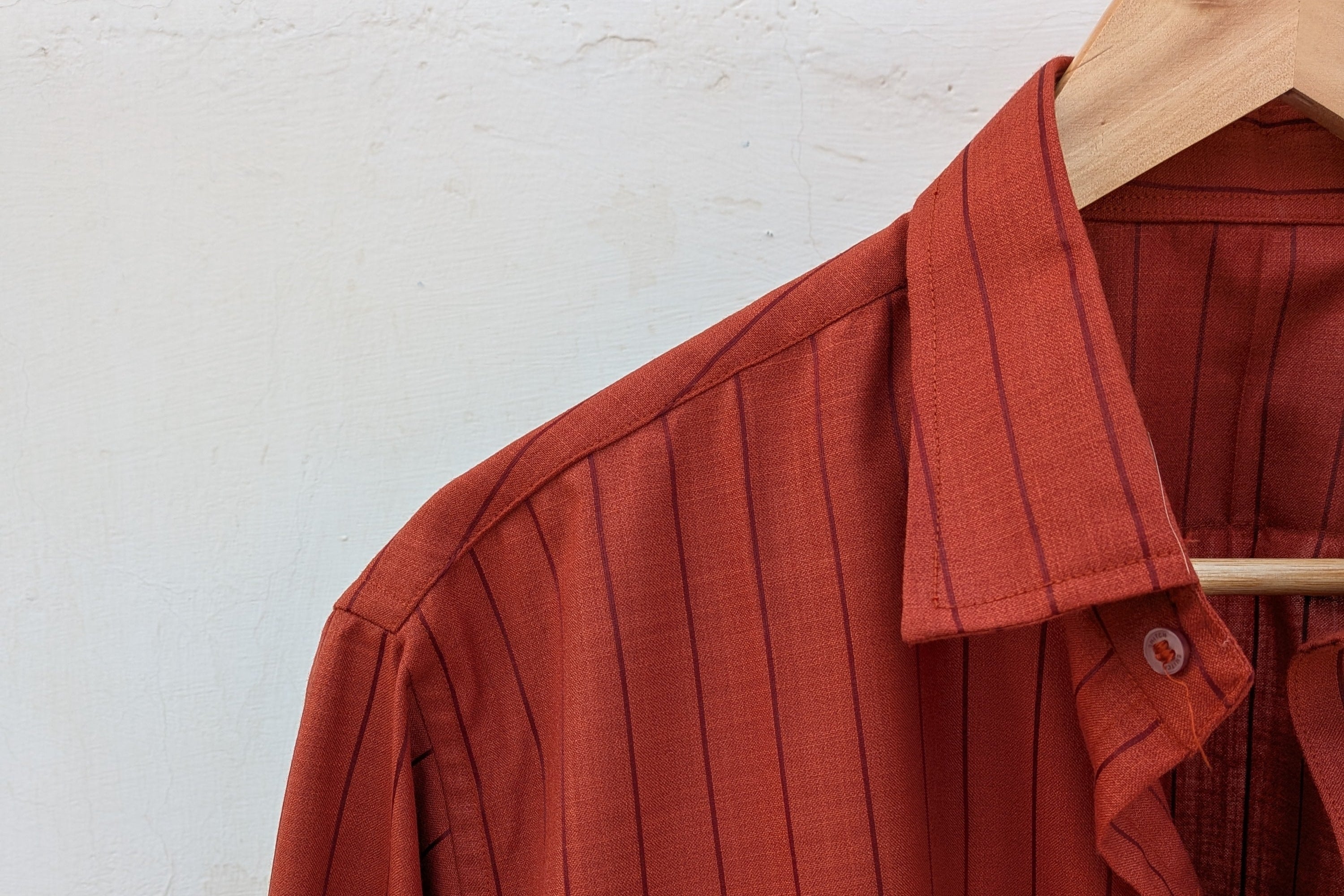 Brown striped shirt on a wooden hanger against a white wall