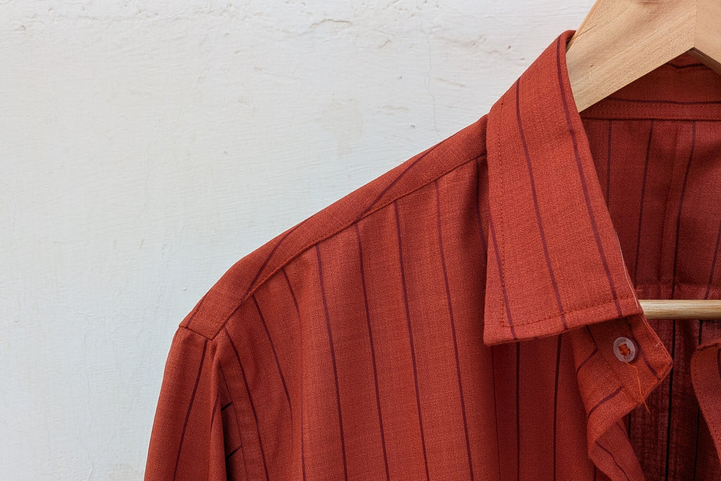 Brown striped shirt on a wooden hanger against a white wall