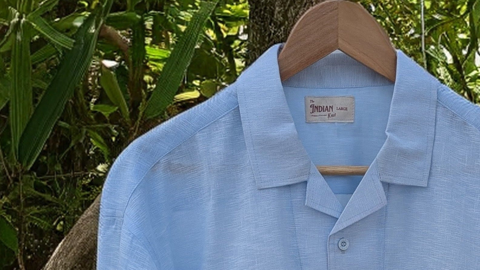 Light blue shirt on a hanger against a natural background of green leaves and branches.