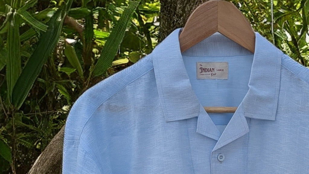 Light blue shirt on a hanger against a natural background of green leaves and branches.